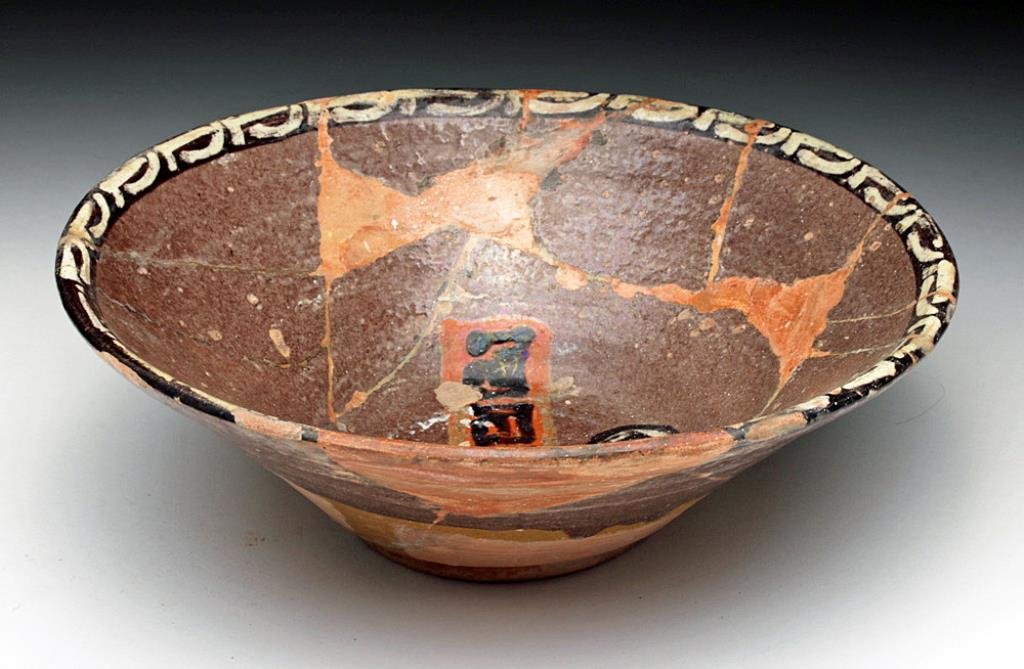 Persian Islamic Pottery Bowl: Iran, 10th to 12th century CE. Decorated pottery bowl with brown walls, band of script down center, scrolls to each side and decorated characters along the rim. 7-1/2" D. Provenance: Ex - D. Smith col