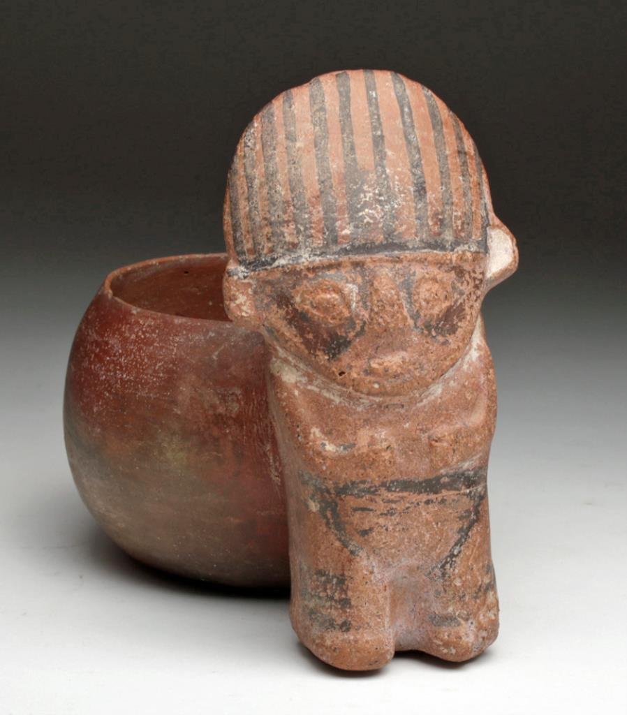 Rare Pre-Colombian Huaco Whistling Cup: Peru, Central Coast, Ca 800 to 1100 CE. Redware vessel in the form of a standing figure, holding hands to his stomach, large striped headband on his triangular head. Incorporated into his backside is