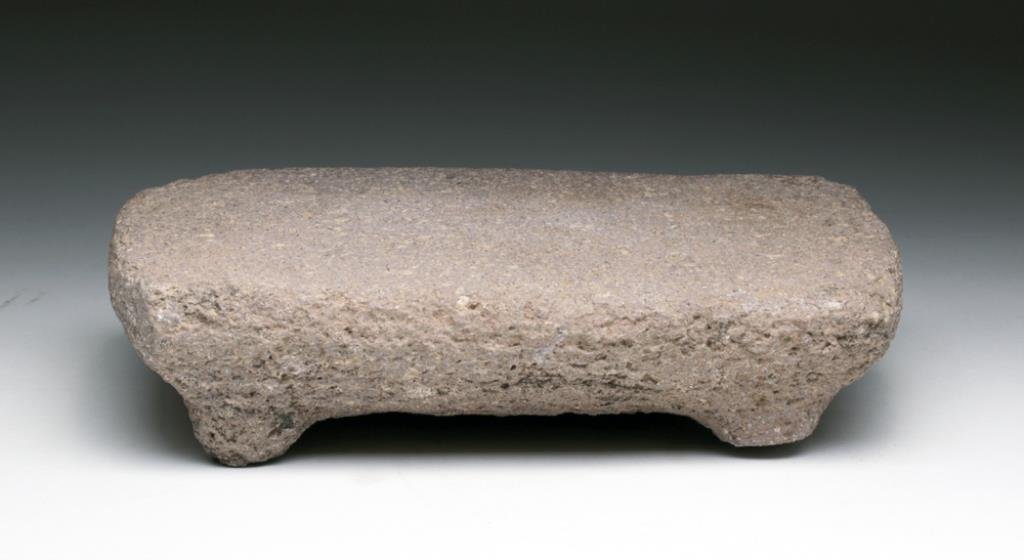 Pre-Columbian Colima Stone Metate: Pre-Columbian, Mexico, Ca 300 BCE to 300 CE. Cute stone metate. rectangular form with very flat top base with 4 nubbin legs, decorative band carved along outside edge. 8-1/2" L. Provenance: Ex Kincade