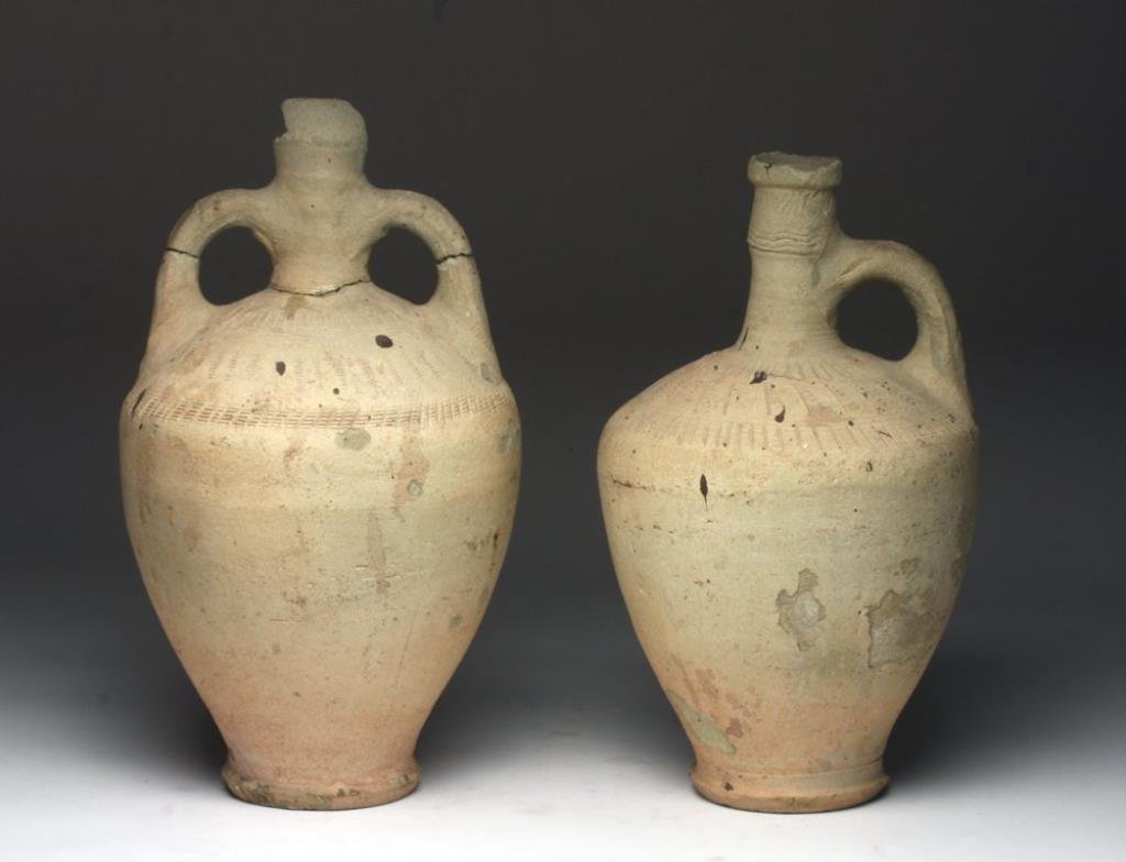 Lot of 2 Near Eastern Spouted Jugs: Ancient Near East. Byzantine or Islamic, ca. 900 - 100 CE. A pair of wheel thrown pottery vessel with pedestal bases, bulbous bodies, tall necks, flared spouts, and strap handles. Each are incised wit