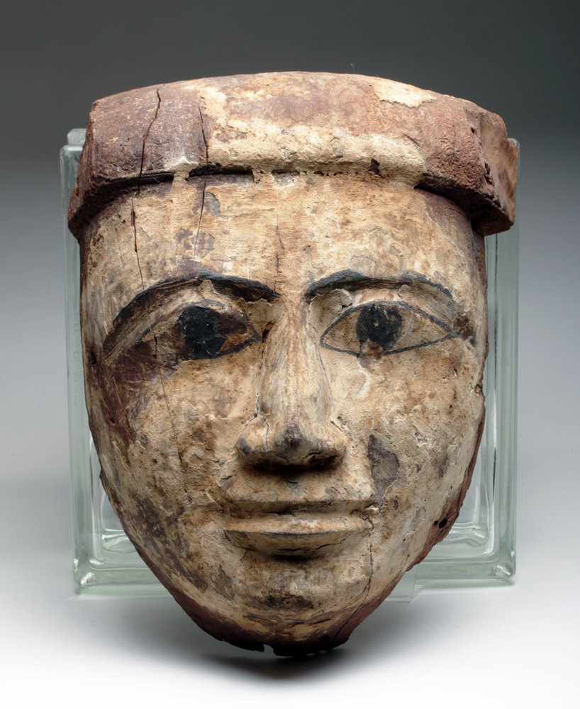 Oversized Egyptian Wood Mummy Mask: Ancient Egypt, ca. 21st/26th dynasty, ca. 1075-600 BCE. Carved from a fine-grained hardwood, the oval/heart-shaped face with finely delineated naturalistic nose and lips, long almond-shaped eyes, and 
