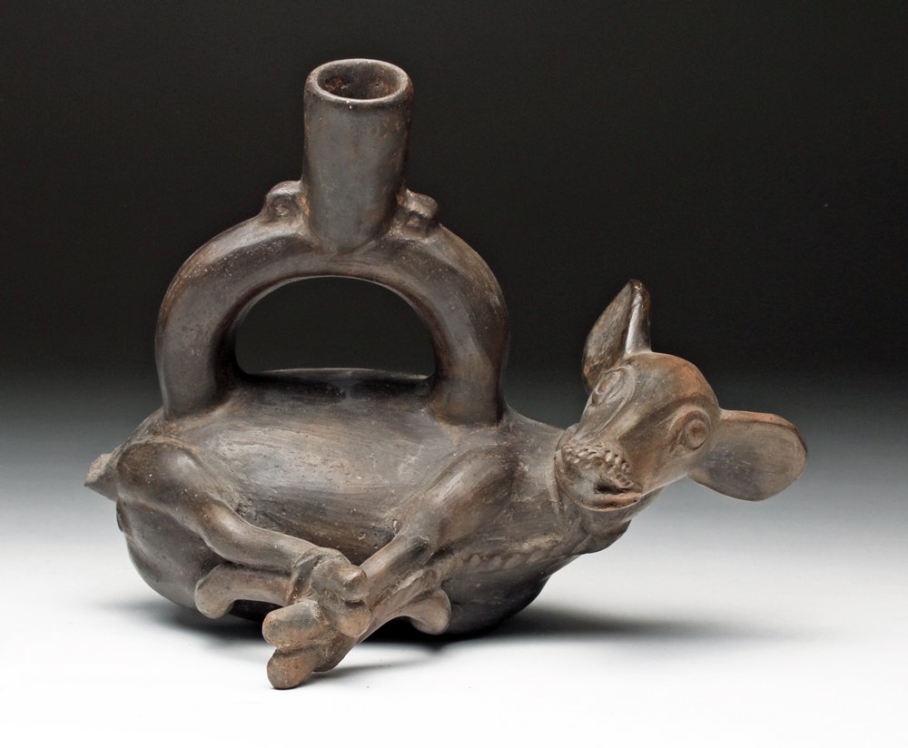Pre-Columbian Chimu Deer Effigy Stirrup Vessel: From ancient Peru, first Chimu phase, ca. 1100 - 1400 CE. Finely-burnished brownware pottery effigy stirrup vessel depicts a captured deer posed on its side, with bound legs. A very artistically advan