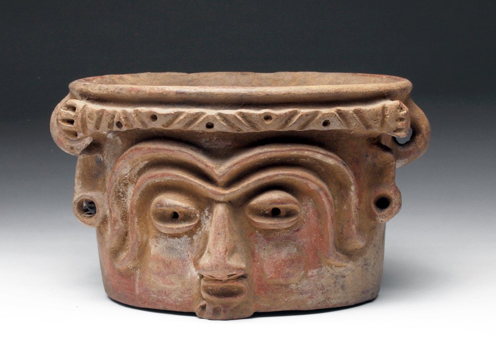 Maya Polychrome Deity Cache Vessel, Applique Molded: Pre-Columbian, Mayan Territories, ca. 400 - 600 CE. A cylindrical deep urn in terracotta with elaborate head of a deity applied, incised and painted to the front. Traces of red and ocher highlights. S