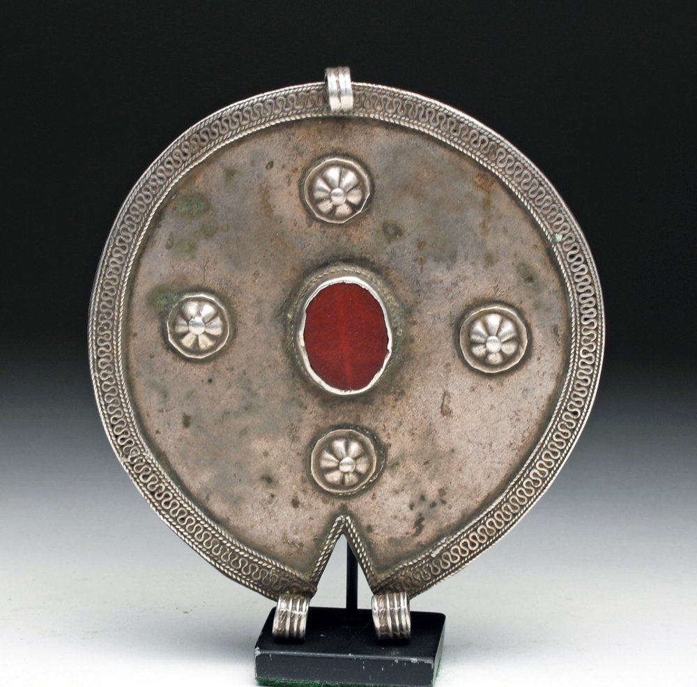 18th C. Asian Silver Pendant w/ Carnelian: Central Asia, ca 18th to 19th century. Large round/slightly oval silver pendant with filigree border and four small appliques of floral forms surrounding a raised inset large oval carnelian stone. Loo