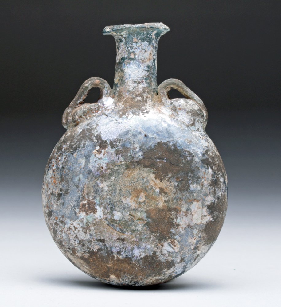 Roman Glass Pilgrim Flask / Canteen: Rome, ca. 2nd - 4th century CE. Ancient glass vessel with free blown lentoid body, a cylindrical neck cinched at its base, the disk rim infolded, the body pinched on either side at center, pair of app