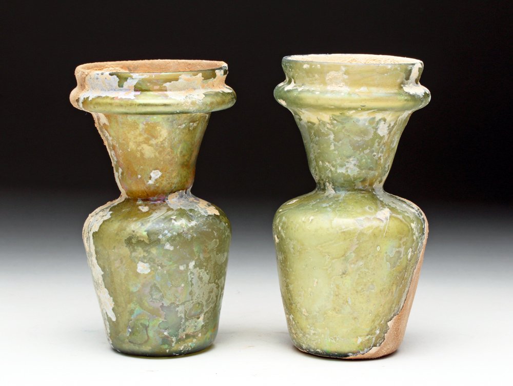 Matched Pr. Roman Glass Bottles: Rome, ca. 1st to 2nd century CE. Matching pair of medium yellow-green glass bottles, each with tapered bodies and wide tooled mouths. Both with areas of strong calcified earthen surface deposits and s