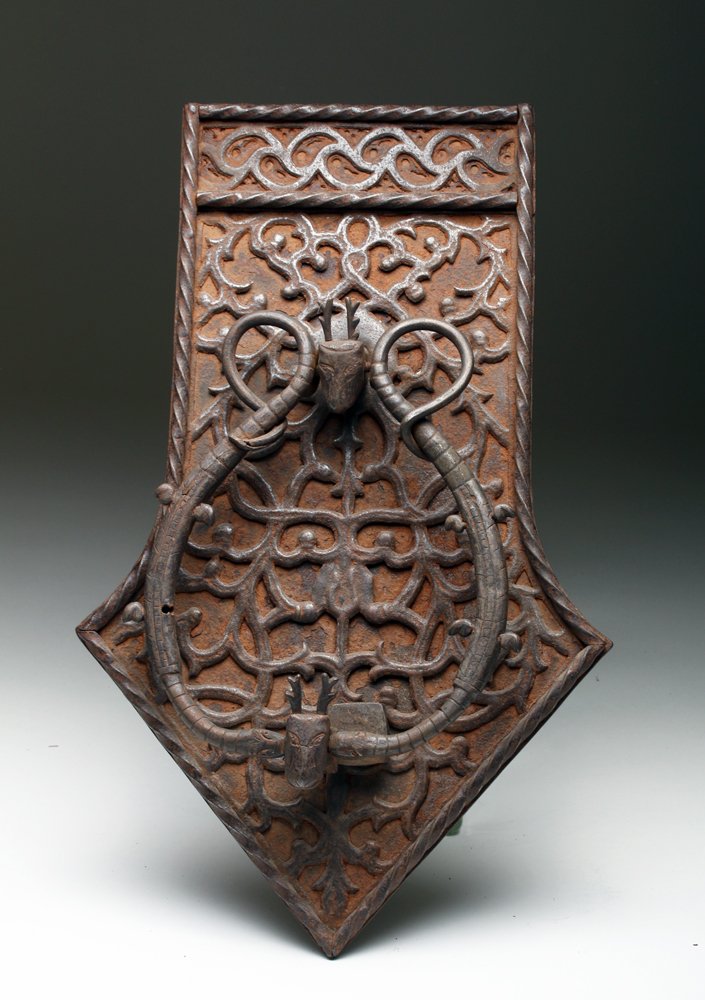 17th C. Spanish Iron Door Knocker: Spain, showing Moorish influence, ca. 17th to 18th century CE. An absolutely stunning and quite amusing iron door knocker. Large iron panel with scrolled decoration, attached to back panel is an emerg