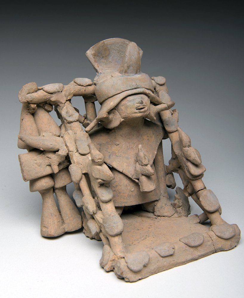 Elaborate Veracruz Terracotta Seated Male Shaman: Veracruz / Vera Cruz, Mexico, ca. 600 to 900 BCE. Elaborate pottery male shaman figure wearing a ceremonial costume standing in a corral with heavily applied disc decorative elements on diagonal slats