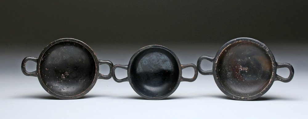Lot of 3 Greek Blackware Kylikes: Magna Graecia, Southern Italy, ca. 4th century BCE. Three lovely blackware kylixi or wine cups, each on a short foot with two horizontal handles and shallow bowls. Size: first measures 6-5/8" (16.8 cm