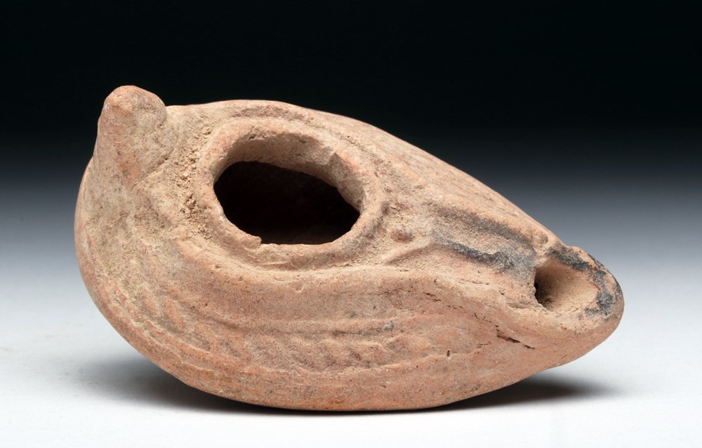 Byzantine Terracotta Oil Lamp: Byzantine, ca. 400 to 600 CE. This fired terracotta lamp has a handle, a hole for pouring in oil, and a hole for the wick and flame to emerge. There is a channel between the two holes and some decorat