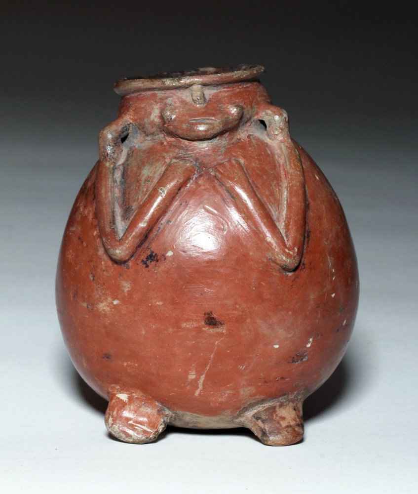 Colombian Negative-Resist Pottery Olla: Pre-Columbian, Colombia, ca. 750 to 1250 CE. This is a burnished red olla with a unique negative resistance carving of a zoomorphic figure with arms raised across his chest; his body forms the olla an