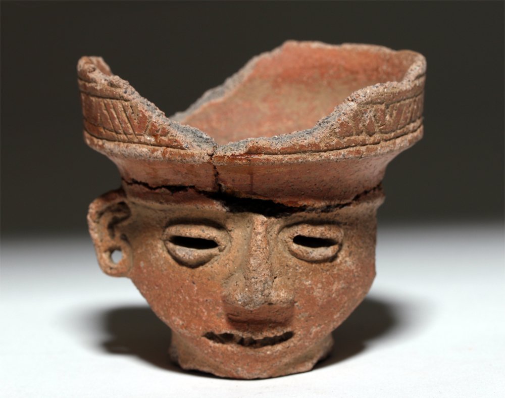 Pre-Columbian Pottery Figural Incensario: Pre-Columbian, ca. 300 to 1500 CE. This is a redware pottery incensario with a small, bowl-like surface for burning. The rim of the bowl has linear and banded decoration. The bowl sits atop a carved h
