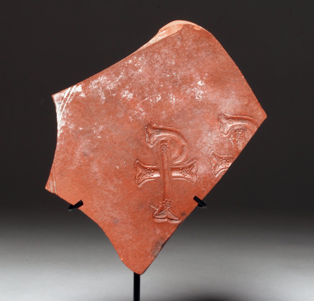 Roman / Byzantine Pottery Fragment with Chi Rho: Roman Byzantium, ca. 4th to 6th century CE. This is a glossy red fragment of pottery that looks like it was once a disc or the bottom of a shallow bowl. One full and one half of a Chi Rho symbol with 