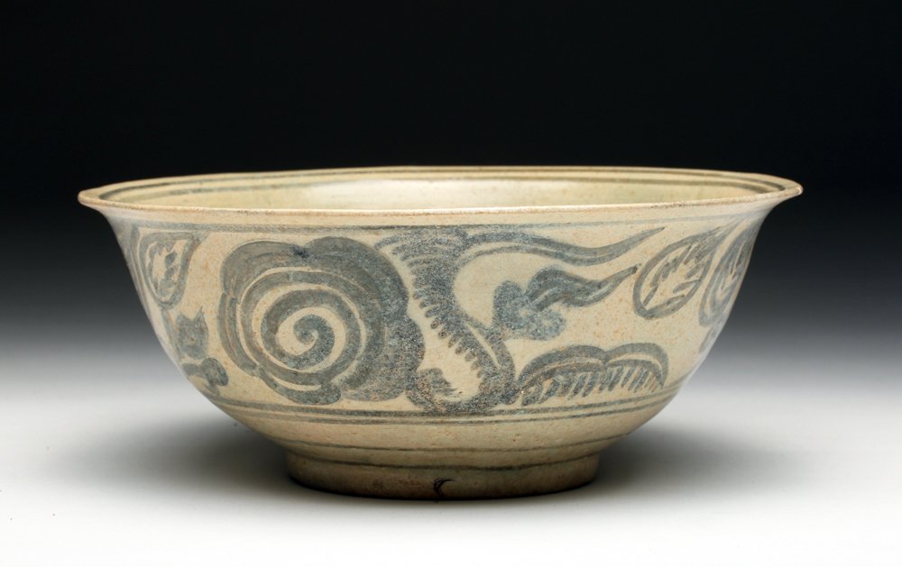 14th C. Sukothai Stoneware Bowl with Floral Motif: Southeast Asia, Thailand, Sukhothai, ca. 1300 CE. Stoneware bowl with floral design on exterior. Interior laid with a cream slip, the central medallion painted in blue glaze, the exterior wall laid wi