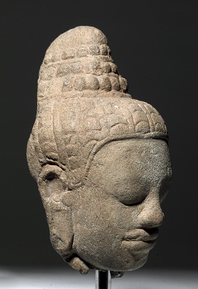 15th C. Cambodian Khmer Stone Head of Buddha: Southeast Asia, Cambodia, Khmer, ca. 15th to 16th century CE. A high relief fragment depicting the head of a Buddha carved with a characteristic Bayon style tiered ushnisha and rashmi. The visage is a