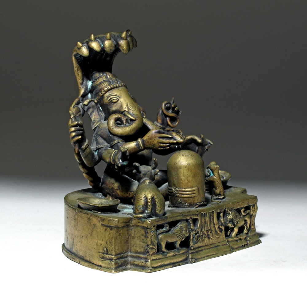 India Ganesha Brass Statue w/ Mouse and Cow: India, early 20th century CE. This is a cast brass statue of elephant-headed Hindu god Ganesha. He is seated, each of his six arms holding a different symbolic item, on an altar before an adoring sacr
