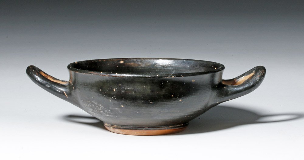 Greek Attic Blackware Kylix - Classic Form: Ancient Greece, Athens, ca. 4th century BCE. A classic blackware kylix with a wide, shallow cup, standing upon a raised ring base, with twin horizontal handles on either side of cup. The monochromatic