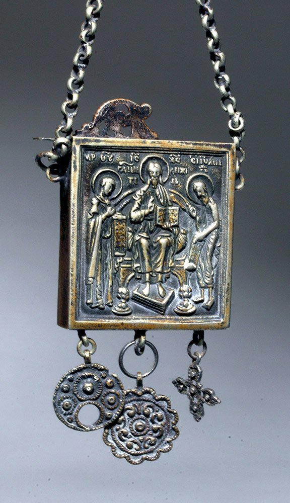 Russian White Metal Reliquary: Russia, 17th to 18th century CE. This is a white metal -- possibly silver -- reliquary on a chain with intricate carved detials and a scene of two apostles and Christ on a throne, all reading from boo