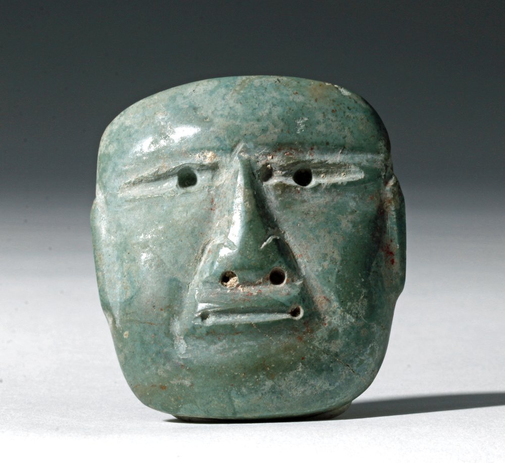 Miniature Olmec Jadeite Maskette: Pre-Columbian, Mexico, Olmec culture, ca. 10th to 6th century BCE. This is a beautiful miniature jadeite mask with a finely detailed, long, straight nose, narrowed eyes with drilled pupils, and a flat