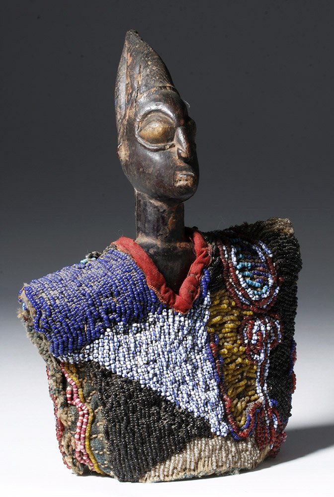 20th C. African Ibeji Carved Wood Male w/ Beaded Cloak: West Africa, Nigeria, Yoruba culture, Ibeji, ca. early 20th century CE. A hand-carved, wooden, nude male figure that stands upon an integral circular base arms at sides and fingers/hands cupped toward