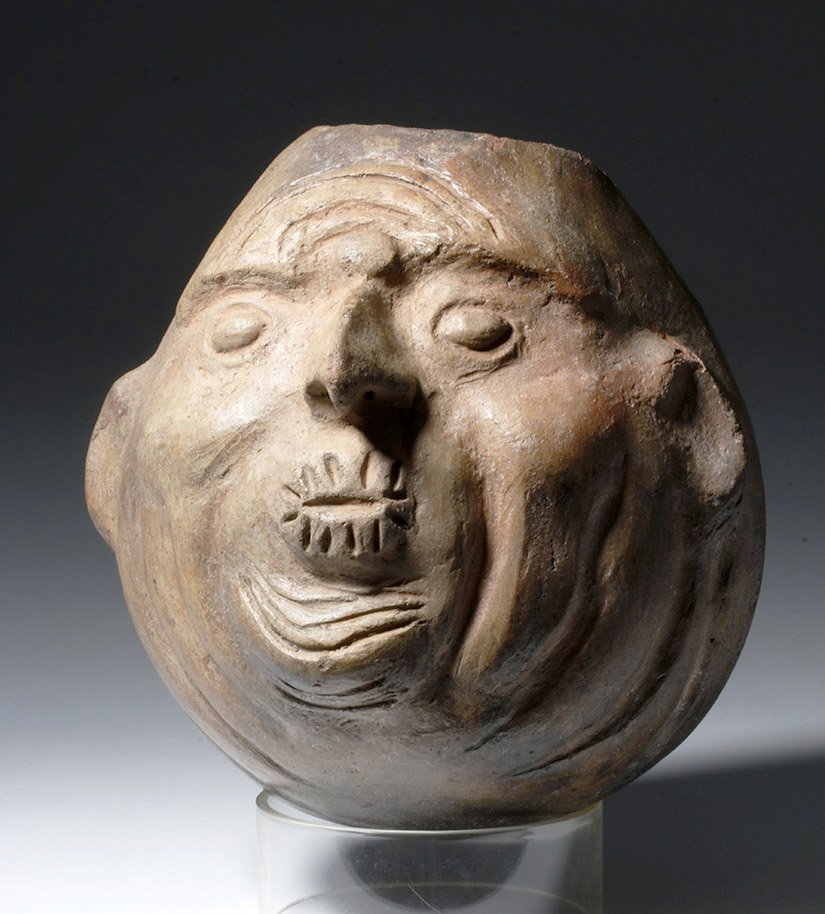 Moche Buff Terracotta Trophy Head Vessel, ex-Museum: Pre-Columbian, North Coast Peru, Moche, ca. 100 to 800 CE. An unusual Mochica terracotta head vessel of a pear-like shape depicting a rather grotesque trophy head, replete with wrinkles across his ent