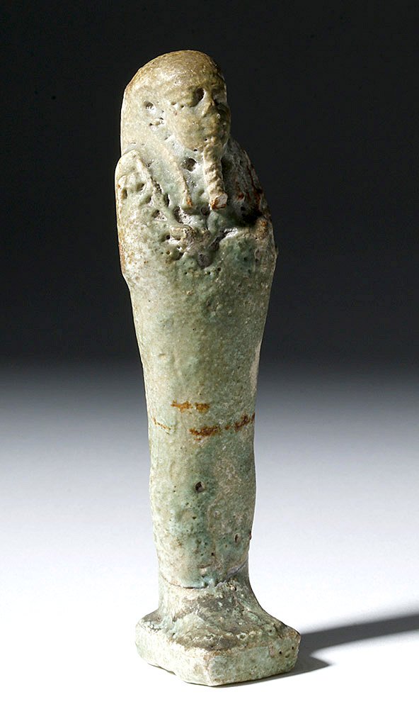 Egyptian Late Period Faience Ushabti: Egyptian, late Dynastic Period, ca. 712 to 332 BCE. This is an ushabti (shabti) with a grey-green faience coating. It has its arms crossed over its chest and is holding hoes (for a clearer photo of a