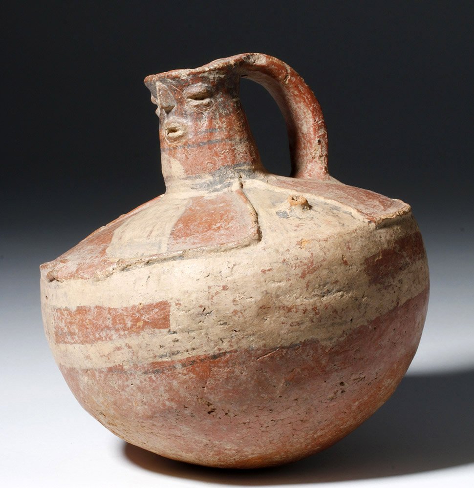 Rare Muisca Pottery Anthropomorphic Bottle: Pre-Columbian, Colombia, South America, ca. 800 CE. Deep bowl on rounded base, overall slip painted and highlighted in red pigment with banded patterns; exterior with effigy head molded into body; fin