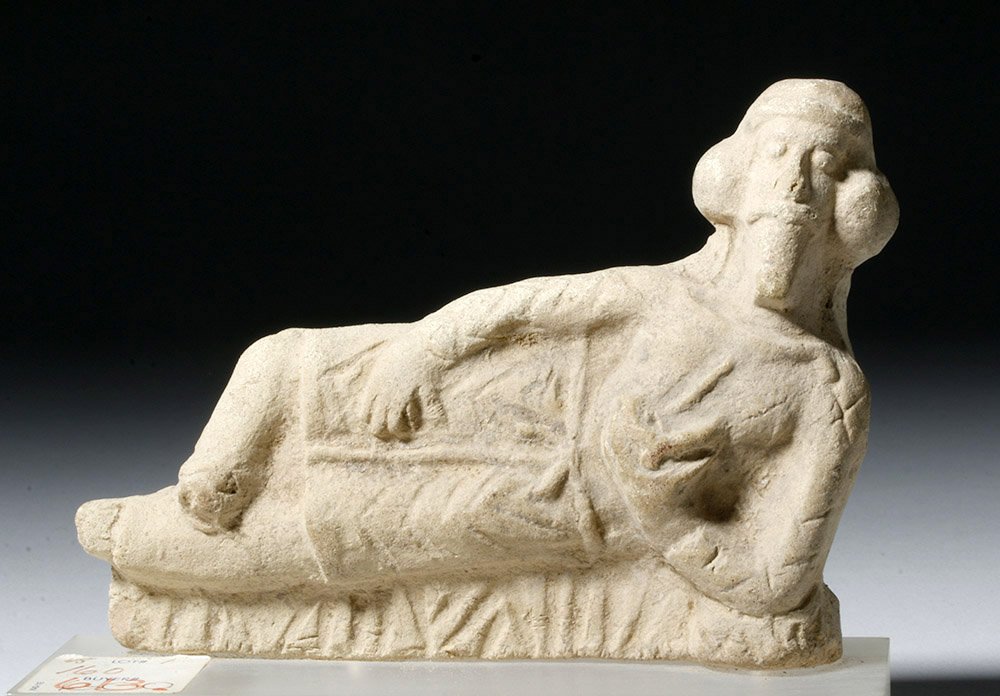 Greek Pottery Banqueter - Reclining Male: Eastern Greek world, ca. 300 BCE. A fine handmade pottery figure showing a reclining man with chevron-decorated robes and wonderful coiffure and facial hair. He lounges, legs crossed, with one hand on