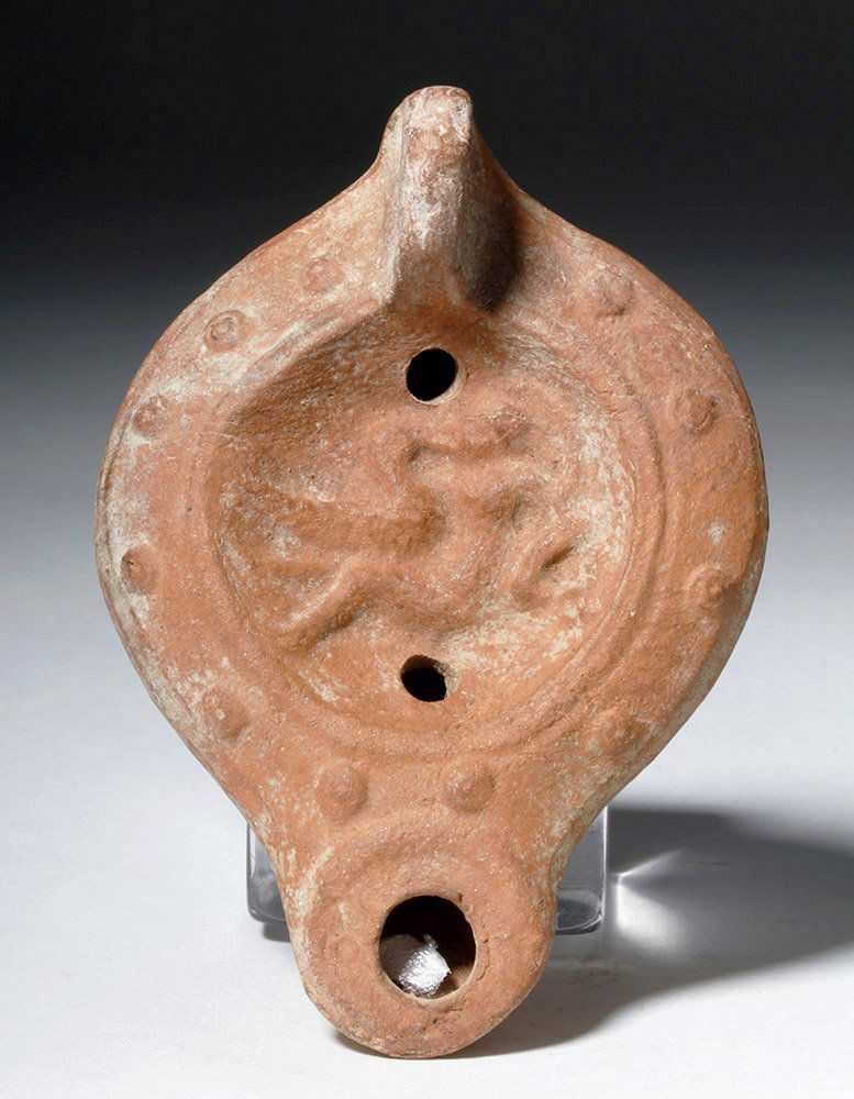 Roman Pottery Oil Lamp - Leda & the Swan: Rome, Imperial Period, ca. 1st to 2nd century CE. This is a redware pottery oil lamp, mold-made, with a stamped design. A short handled and small spouted example, with a low-relief depiction of Leda a