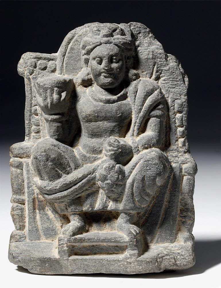Gandharan Stone Carving of Seated Buddha: Pakistan and Afghanistan, Gandharan Empire, ca. 1st century CE. This is a fine example of a Gandharan stone carving; it shows a seated Siddhartha Gautama, richly decorated on a throne and holding item