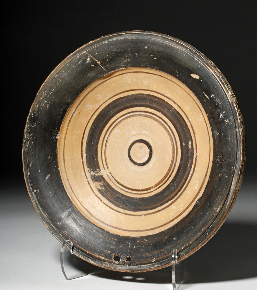 Greek Daunian Pottery Plate: Southern Italy, Apulia / Daunian, ca. 300 BCE. A skillfully wheel-thrown, bi-chrome pottery plate with a relatively high foot and graceful, convex rim. While usually a simple form, this particular pla