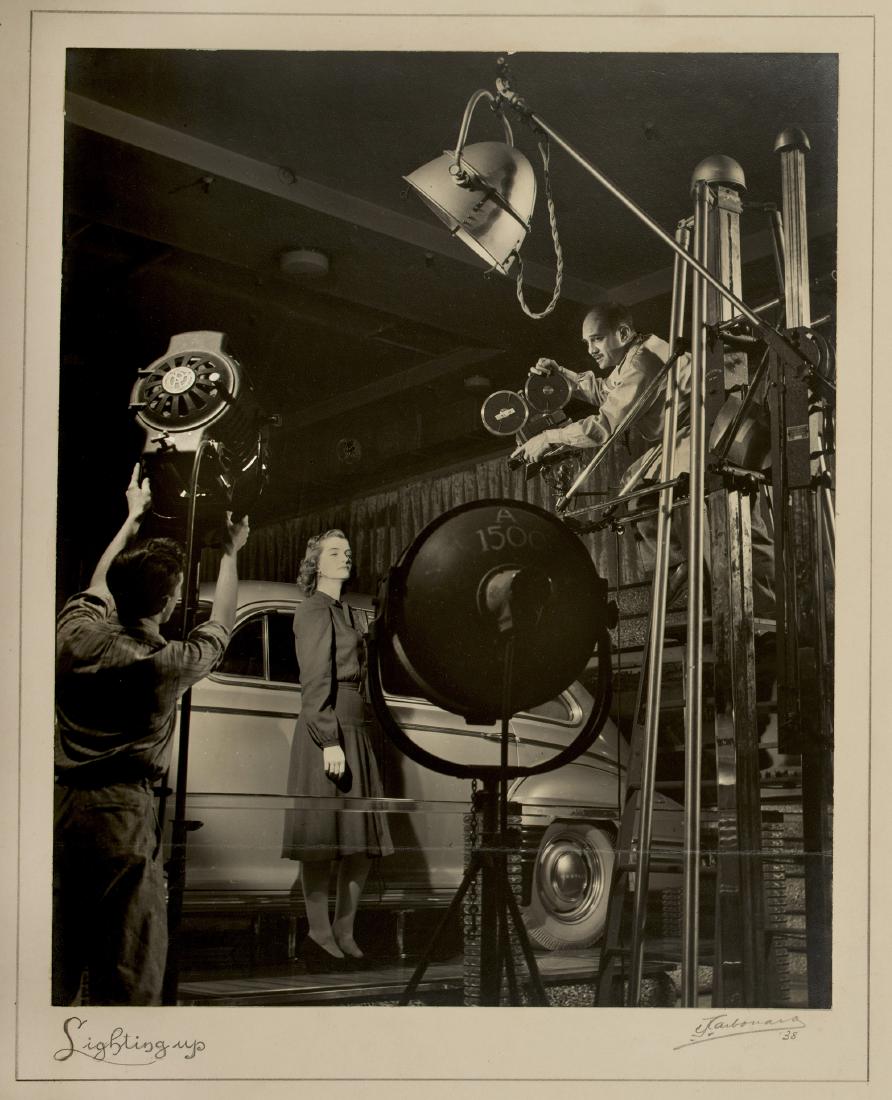 WOMAN IN CAR COMMERCIAL BY CHARLES CARBONARA, SIGNED: Lights! Action! Cameras! Entitled "Lighting up" and signed by the artist at lower right, along with the year: "'38" (1938). Mount is 19 x 16 inches. Photo has a horizontal crease across it (not the mo