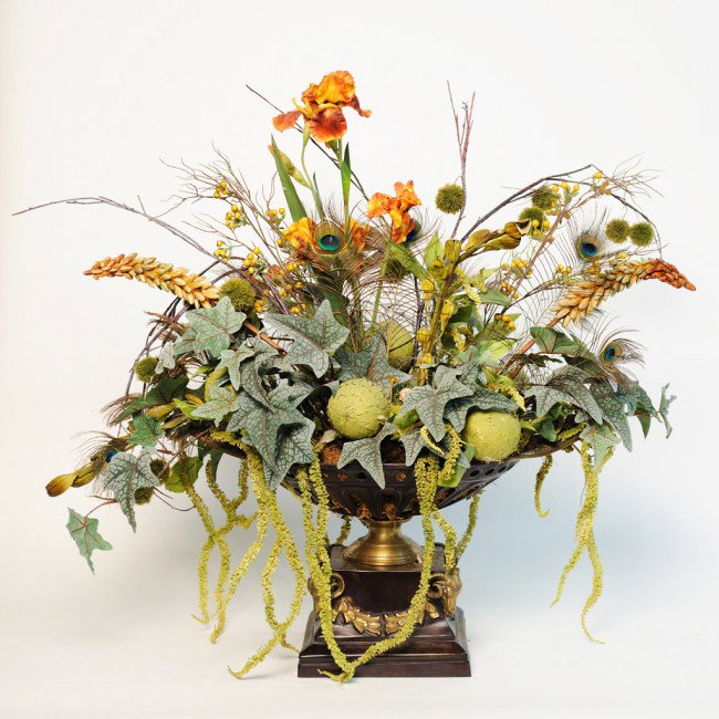 A SILK FLOWER CENTERPIECE WITH ARTICHOKES, DEEP RUS: A SILK FLOWER CENTERPIECE WITH ARTICHOKES, DEEP RUSSET IRISES AND PEACOCK FEATHERS in brass oval pierced base with gilded rams heads 39 x 39 x 21 inches