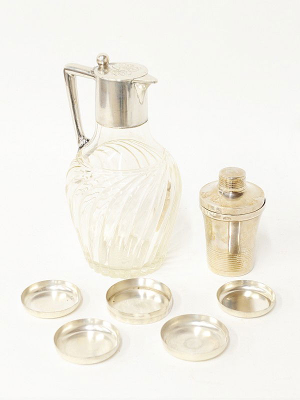 A STERLING MOUNTED SYRUP JUG WITH COCKTAIL SET: A STERLING MOUNTED SYRUP JUG ALONG WITH DESNY COCKTAIL SET syrup jug lid monogrammed with swirl glass body. Cocktail set includes shaker, 3 graduated coasters and nut dish.