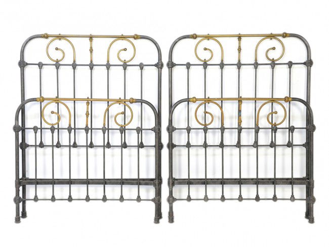 A PAIR OF TEXAN IRON AND BRASS TWIN BEDS: A PAIR OF TEXAN IRON AND BRASS TWIN BEDS the rounded rectangular headboard and footboard having a brass tube with knob terminals crest above, a waisted brass column and flanked by brass scrolls termin