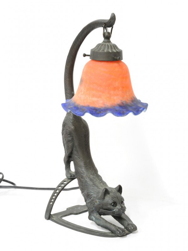 A GREEN AND BLACK PATINATED SPELTER TABLE LAMP, Twe: A GREEN AND BLACK PATINATED SPELTER TABLE LAMP, Twentieth Century sculpture of a stretching cat with glass eyes and a floral bell faux art glass shade hanging from his tail. 16 x 7 x 6 1/4 inches