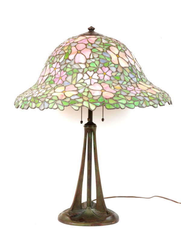 A TIFFANY STYLE LAMP WITH FAUX ART GLASS SHADE, USA: A TIFFANY STYLE LAMP WITH FAUX ART GLASS SHADE, USA Twentieth Century Art Deco inspired patinated metal three legged base. 25 x 21 x 21 inches