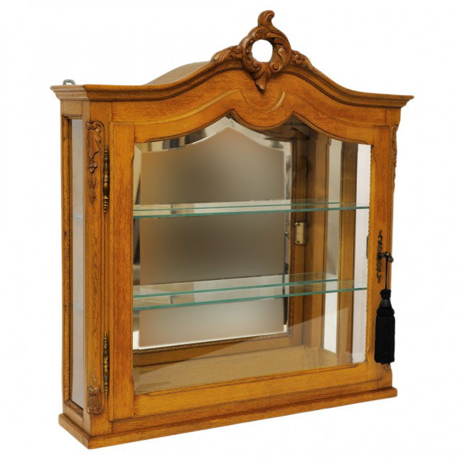 A FRENCH COUNTRY OAK CURIO WALL CABINET: A FRENCH COUNTRY OAK CURIO WALL CABINET with mirrored back, glass shelves and beveled glass doors. some chipping to shaped oak veneered top. 34 x 30 1/2 x 8 inches