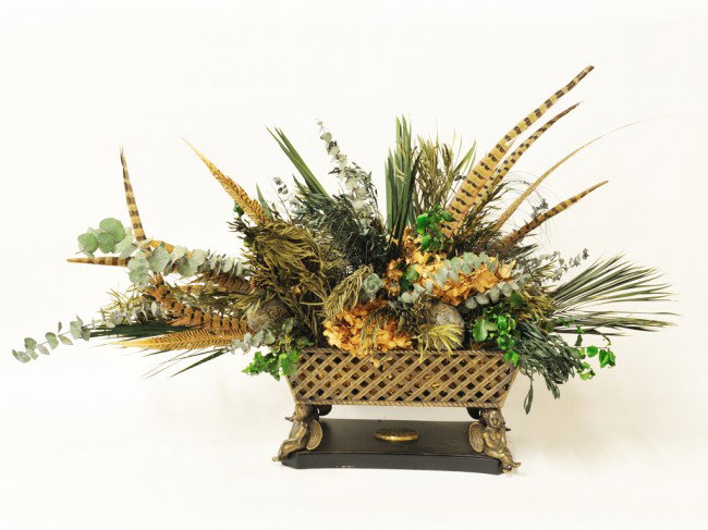 A DRIED FLORAL CENTERPIECE WITH FEATHERS: A DRIED FLORAL CENTERPIECE WITH FEATHERS on a lattice brass base supported by cherubs 19 x 3 x 11 inches