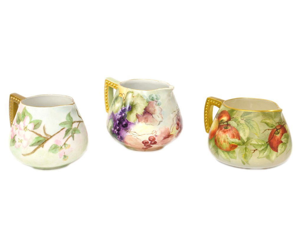 THREE HAND PAINTED AND GILT DECORATED PITCHERS, Ear: THREE HAND PAINTED AND GILT DECORATED PITCHERS, Early Twentieth Centuryone marked ""Hohenzollem China / Germany"" to base; one unmarked and one signed ""JMP 1903"" 3 pieces 6 x 6 1/2 x 7 1/2 inches