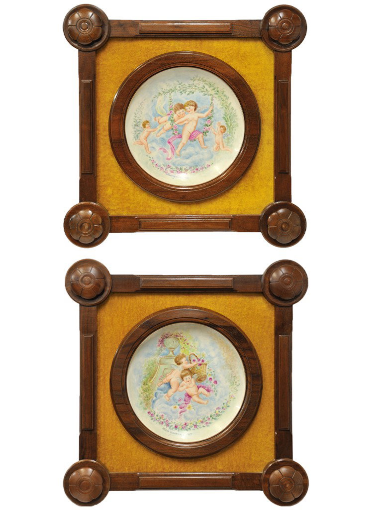 A PAIR OF VICTORIAN HAND CARVED WALNUT FRAMED HAND : A PAIR OF VICTORIAN HAND CARVED WALNUT FRAMED HAND PAINTED PORCELAIN CHARGERSdepicting frolicking putti; both signed and dated Hilde Gavenas, 1987the walnut frames have antique elements 21 x 21 x 3 in