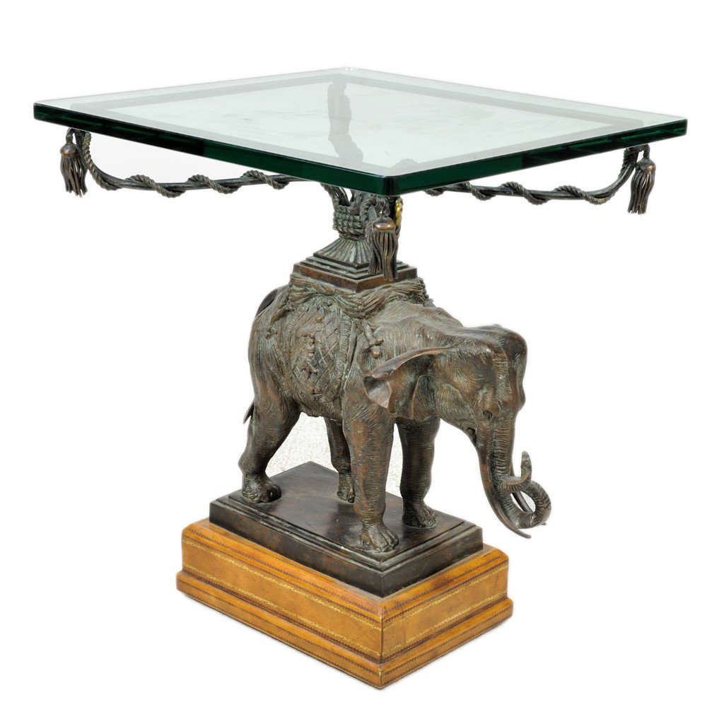 AN ELEPHANT FIGURED PATINATED METAL AND GLASS SIDE: AN ELEPHANT FIGURED PATINATED METAL AND GLASS SIDE TABLE, Late 20th Century the elephant sculpture standing four square on beveled plinth base with his trunk raised and his howdah sporting four twiste