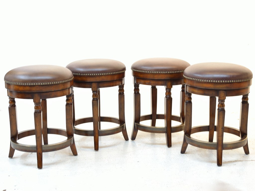 A GROUP OF FOUR LEATHER SWIVEL BAR STOOLS WITH NAIL: A GROUP OF FOUR LEATHER SWIVEL BAR STOOLS WITH NAILHEAD TRIM ON WALNUT STAINED BASE MADE BY ARTISTICA 25 x 18 x 18 inches