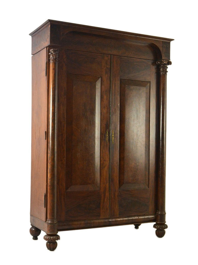 AN AMERICAN LATE CLASSICAL MAHOGANY ARMOIRE: AN AMERICAN LATE CLASSICAL MAHOGANY ARMOIRE Mid-19th century. With a large stepped cornice and broad doors flanked by corinthian columns. Note: one corinthian decorative element missing from letf colu