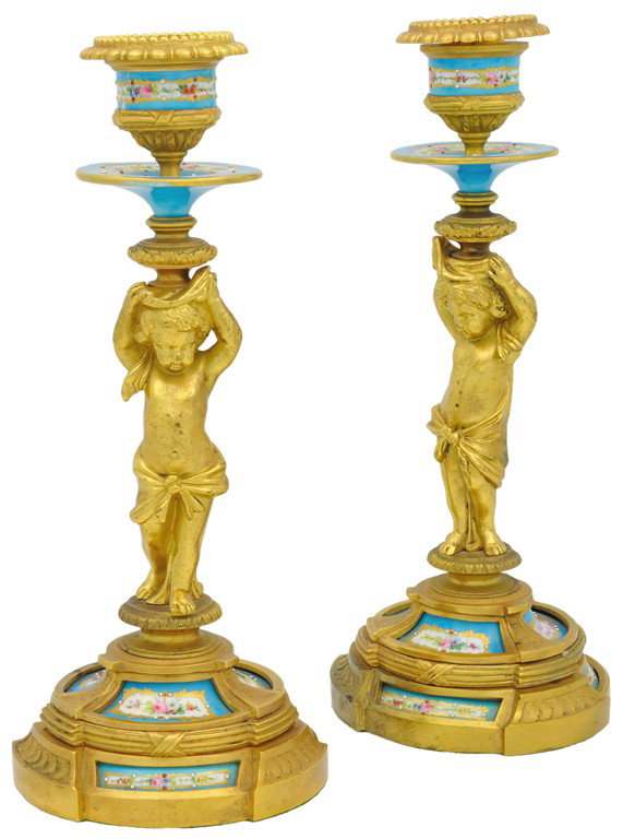 A PAIR OF BRONZE DORÉ AND SÈVRES STYLE PORCELAIN FI: A PAIR OF BRONZE DORÉ AND SÈVRES STYLE PORCELAIN FIGURAL CANDLESTICKS, Late 19th Century Each candlestick featuring a bronze doré putto holding aloft a porcelain candle cup and bobeche while standi