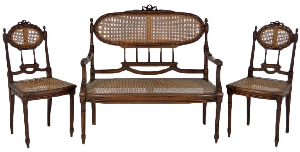 A LOUIS XVI STYLE WALNUT CANE BACK AND SEAT SETTEE: A LOUIS XVI STYLE WALNUT CANE BACK AND SEAT SETTEE AND TWO SIDE CHAIRS The oval ribbon and rod carved detail is surmounted by a crenelated bow and surrounds hand-caned reserves; the backs are supporte