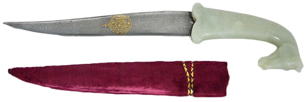A MUGHAL STYLE JADE HANDLED DAGGER: A MUGHAL STYLE JADE HANDLED DAGGER 20th Century Jade carved horse head handle with decorated steel blade. Velvet scabbard with decorative cord wrap. 15 x 3½ x 1 inches
