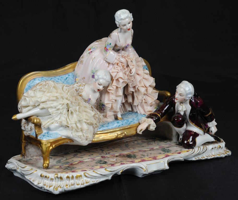 A COURTLY ITALIAN PORCELAIN FIGURAL GROUP: A COURTLY ITALIAN PORCELAIN FIGURAL GROUP 1st quarter 2th Century Depicting two women and a man in late eighteenth century dress flirting, the women on a couch and the man kneeling on a floral carpet,