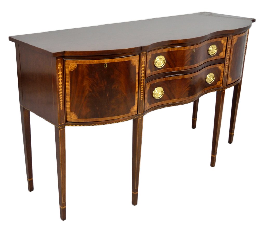 A SHERATON STYLE MAHOGANY SIDEBOARD BY COUNCIL CRA: A SHERATON STYLE MAHOGANY SIDEBOARD BY COUNCIL CRAFTSMAN 20th Century Serpentine shaping with two doors flanking two drawers, raised on slender tapered block legs. Ribbon mahogany bands the drawers an