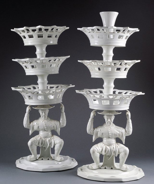 A PAIR OF PORTUGUESE BLANC DE CHINE CENTER PIECES P: A PAIR OF PORTUGUESE BLANC DE CHINE CENTER PIECES Portugal, Mid-20th Century The Allgre Vista three tier center pieces feature a whimsical Chinese Man crouching and supporting three tiers of graduated